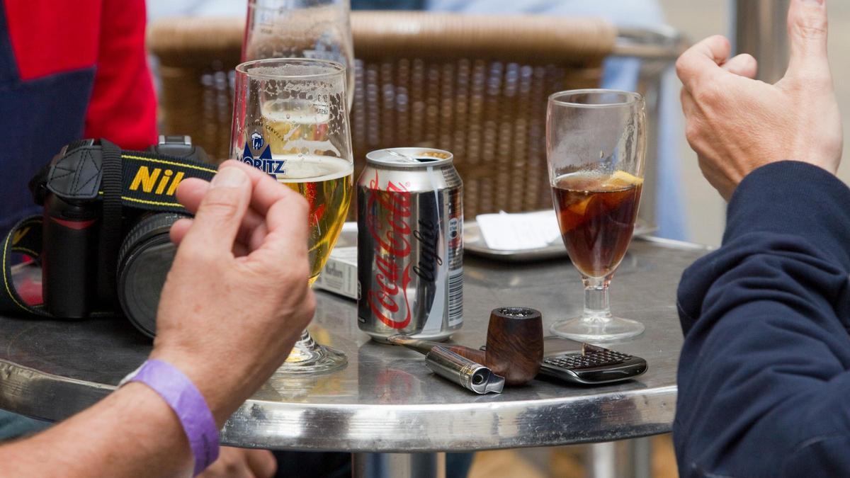 Dos personas se toman unas consumiciones en una terraza de la plaza del Rei de Barcelona con una cámara de fotos y un móvil, entre otras cosas, encima de la mesa.