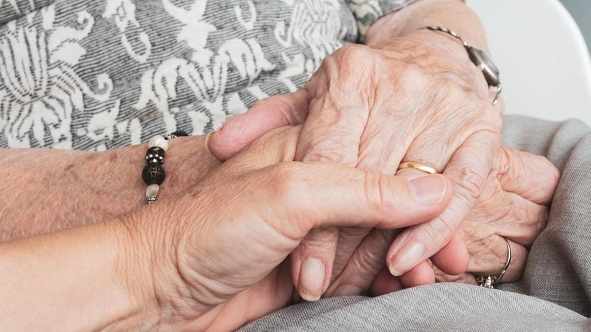 Una persona coge la mano de una anciana.