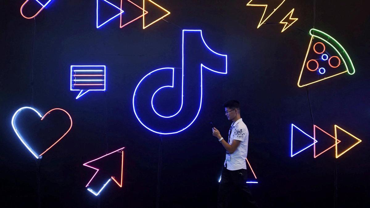 Un hombre mira su teléfono móvil mientras pasea frente el logo de TikTok