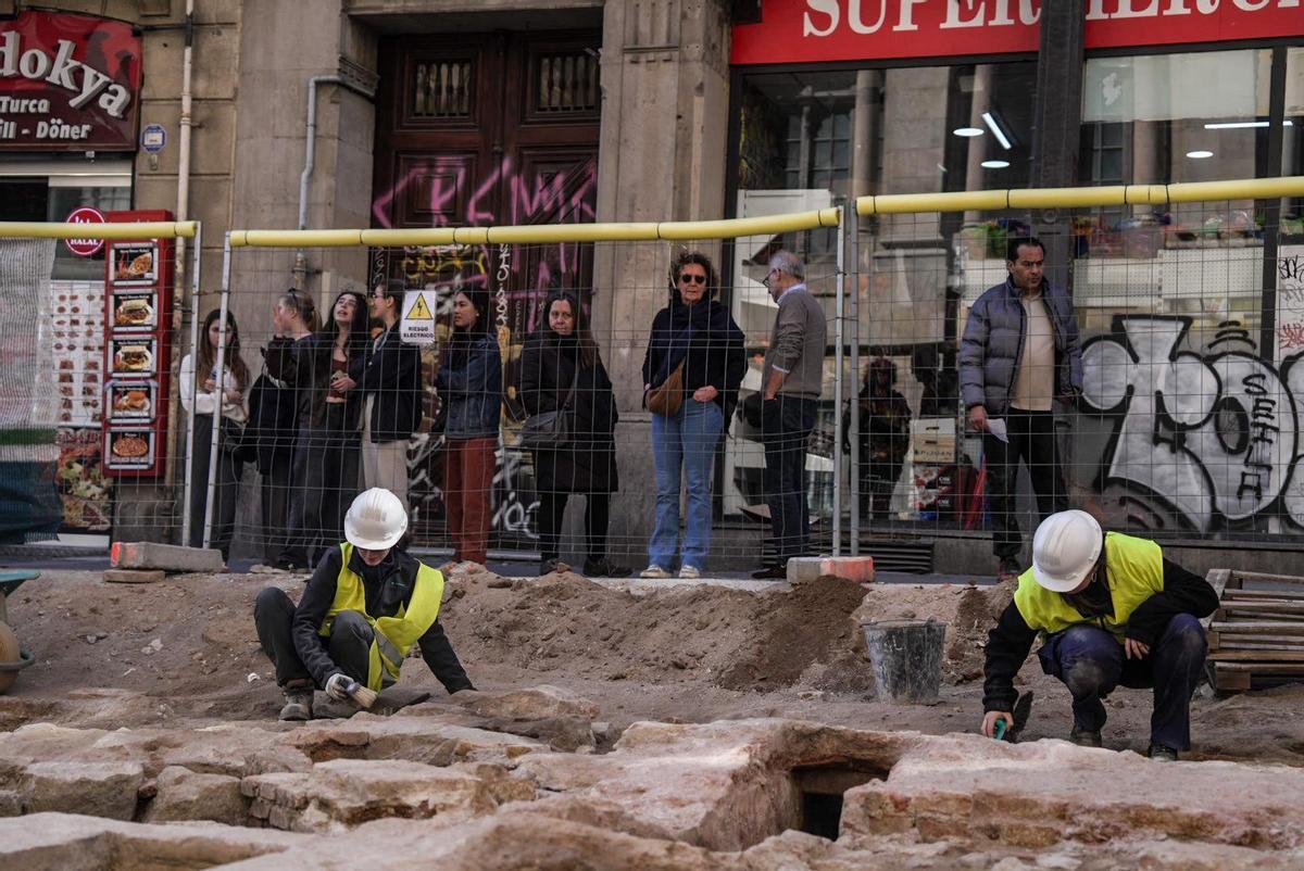 Certains piétons observent les explorations archéologiques de la rue Fusteria, à Barcelone.