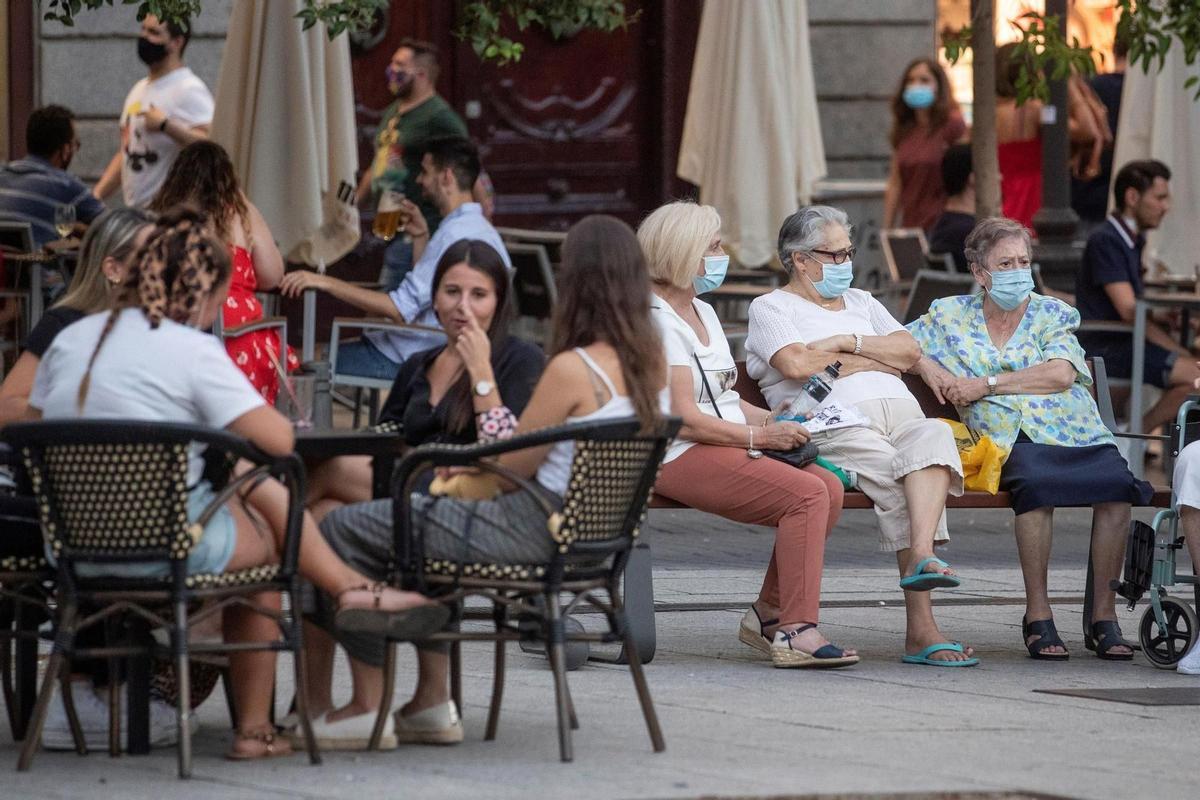 Des personnes âgées dans une banque et des jeunes sur une terrasse, à Pedro Zerolo Square à Madrid, en août 2020.