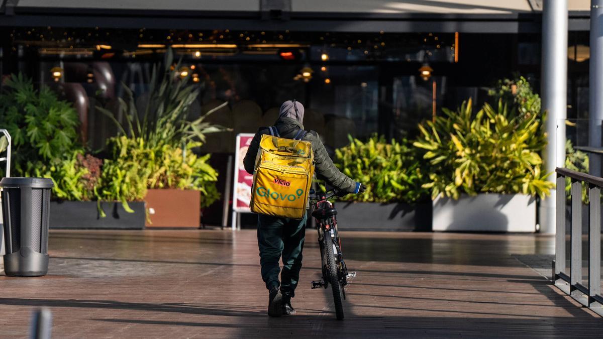 Repartidores de comida a domicilio de la empresa Glovo esperan, recogen y reparten comida en el centro comercial La Maquinista.