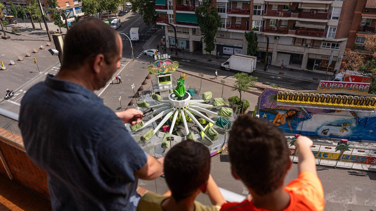 Un padre y dos de sus hijos observan un par de las atracciones de la feria de la fiesta mayor de Sants, en Barcelona.
