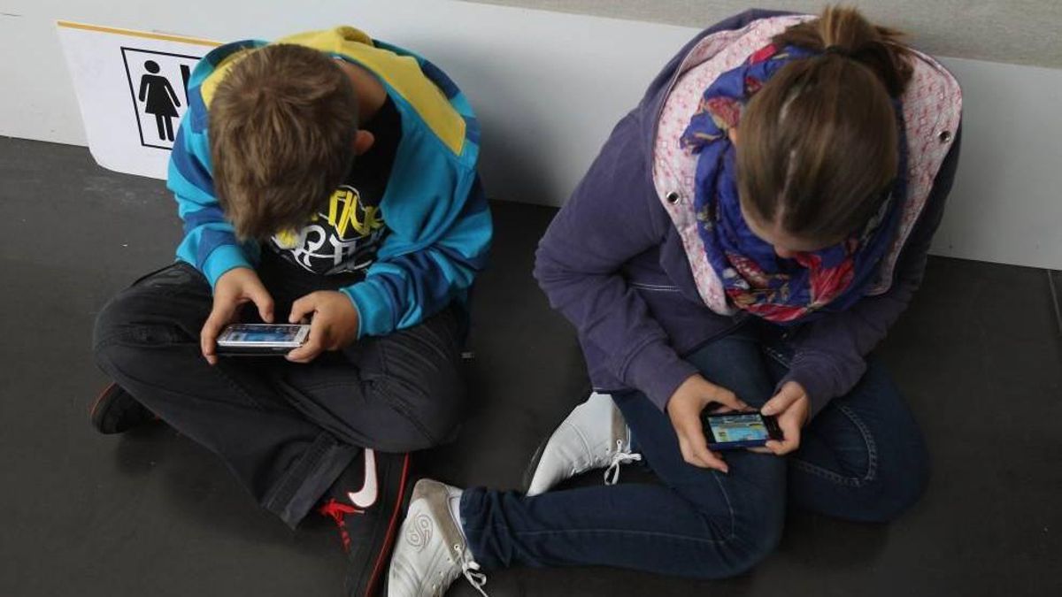 Dos adolescentes miran sus teléfonos móciles.