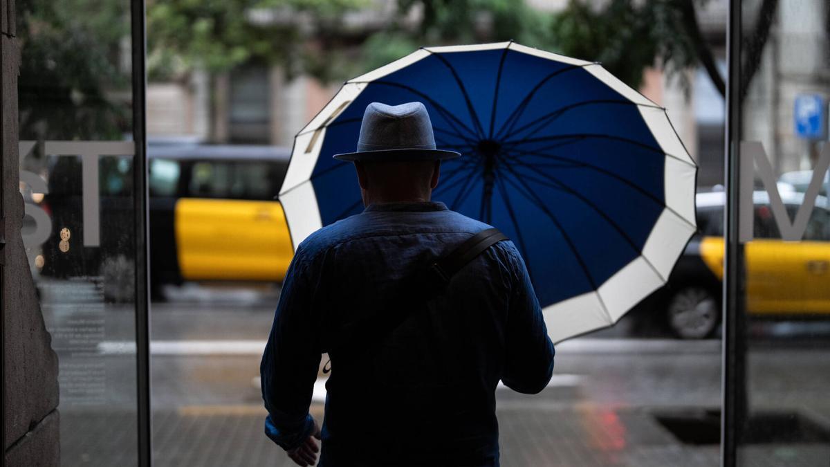 Turistas y locales se protegen de la lluvia con paraguas y chubasqueros. Lluvia en el centro de Barcelona.