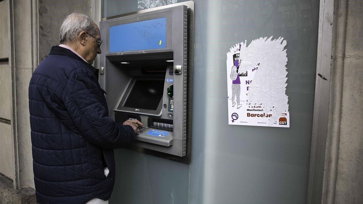 Un pensionista saca dinero en efectivo de un cajero automático de una entidad bancaria de Barcelona.