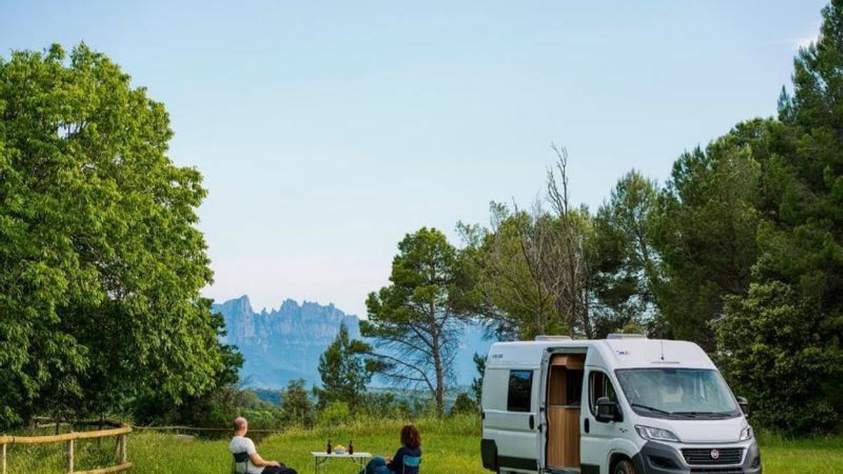 Una pareja desansa al lado de su cámper contemplando unas montañas.