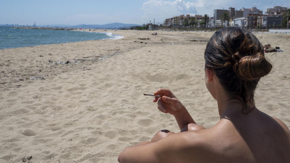Una joven sostiene un cigarrillo en la playa del Pla de l’Ós en Premià de Mar