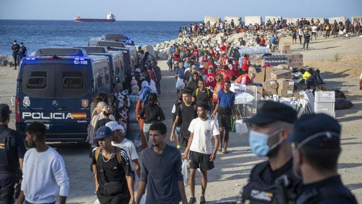 Agentes de la Policía Nacional y miembros de Cruz Roja, con los inmigrantes acampados en la playa del Trampolín de Ceuta.