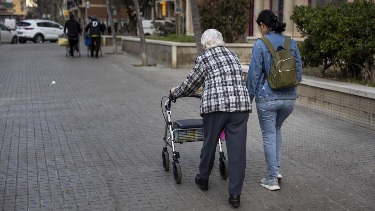 Una persona mayor dependiente pasea junto a su cuidadora.
