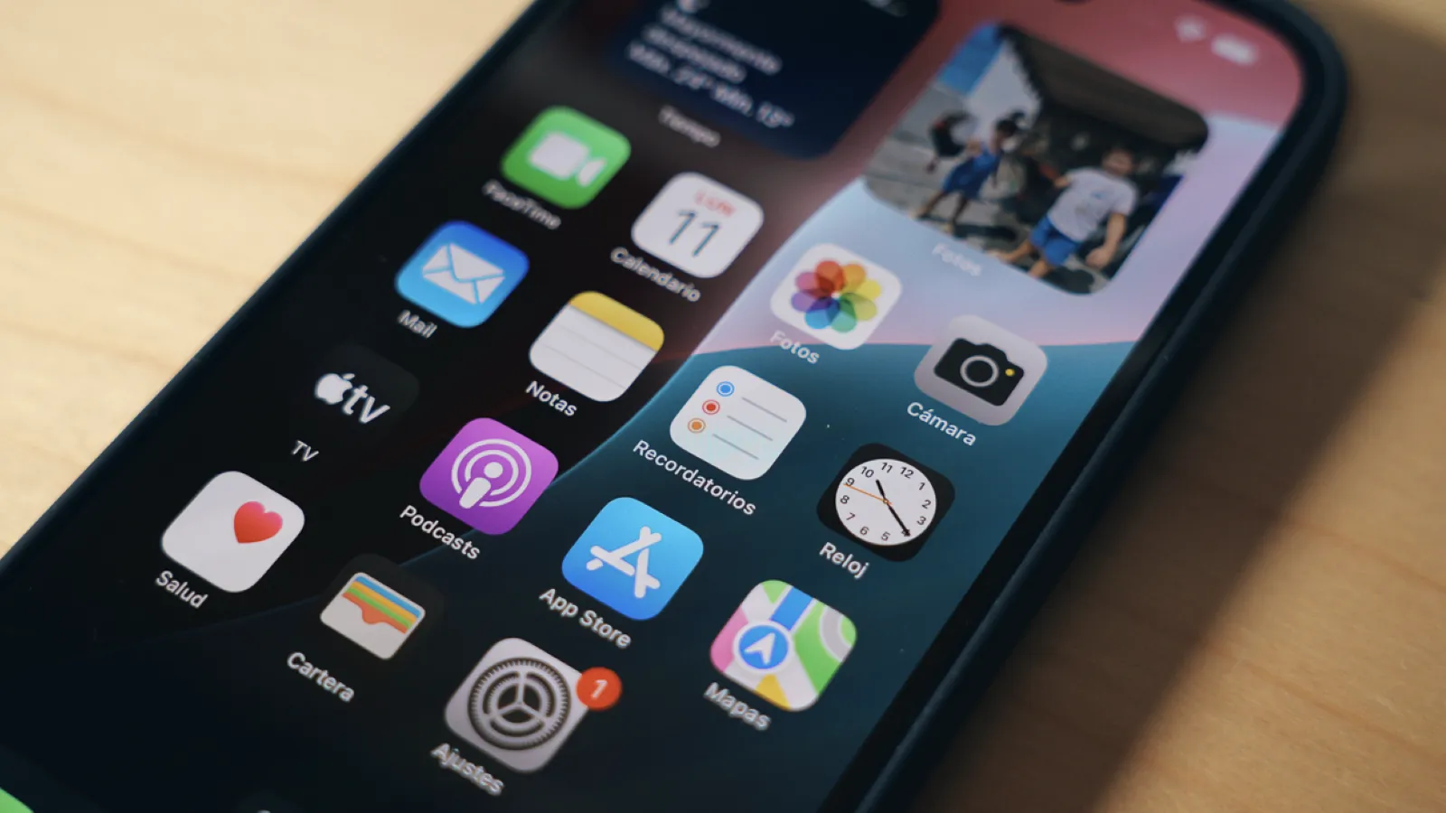 Gros plan de l'écran d'un iPhone 16 avec diverses icônes d'applications système iOS disposées sur l'arrière-plan du bureau.