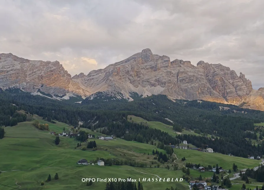 Massif montagneux des Dolomites sous un ciel nuageux avec des prairies verdoyantes dans la vallée.