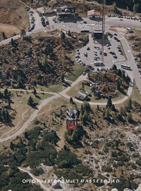 Vue aérienne d'un téléphérique remontant un versant de montagne vers un parking et une station de base.