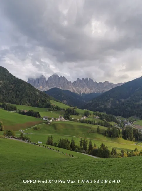 Paysage de montagne avec des sommets abrupts sous un ciel nuageux et des vallées de prairies verdoyantes.