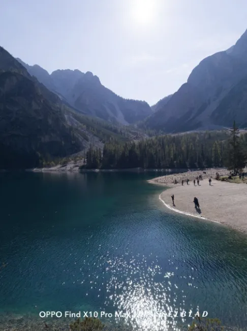 Lac de montagne aux eaux turquoise et reflets du soleil à côté d'une rive sablonneuse avec des gens.