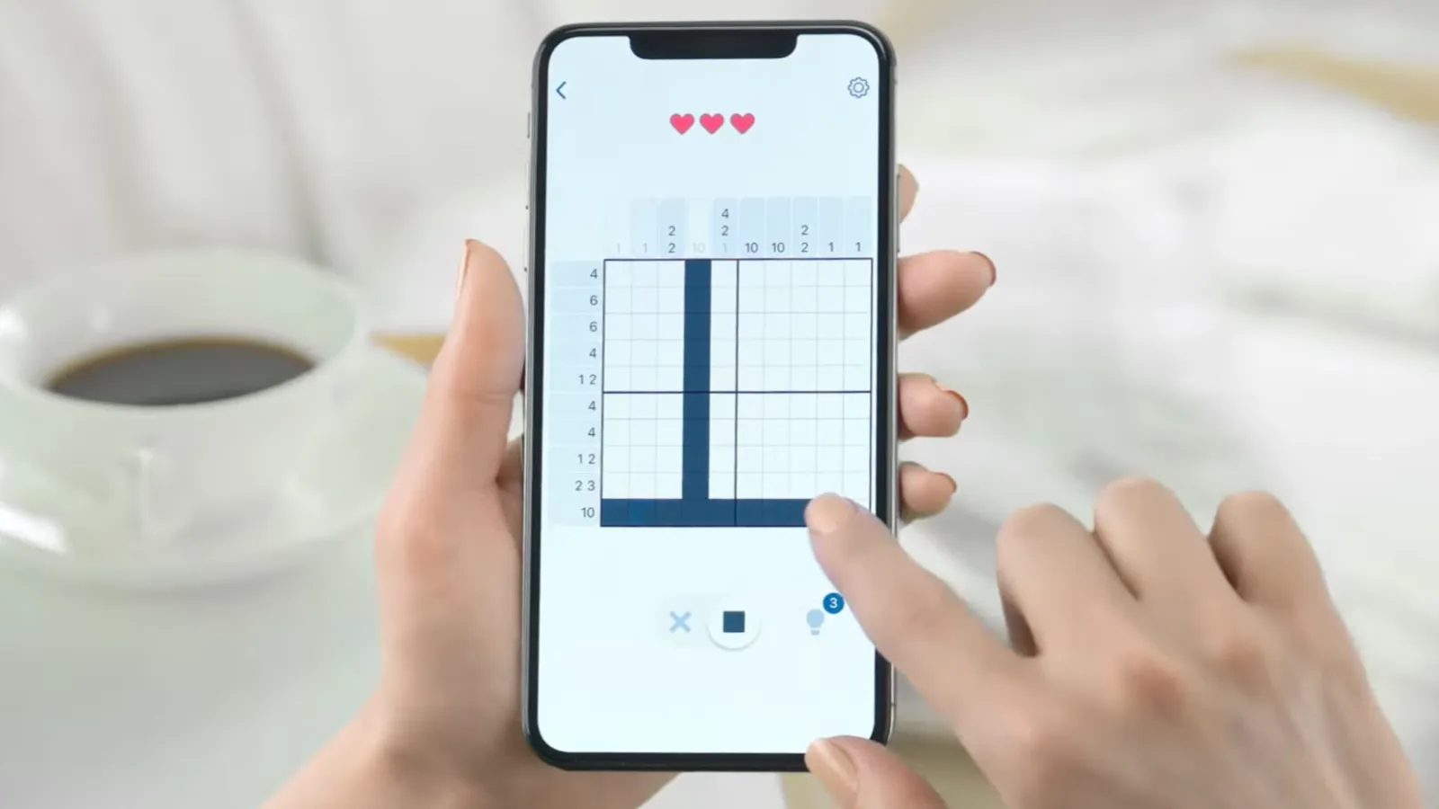 Personne jouant un nonogramme sur un smartphone sur une table avec une tasse de café.