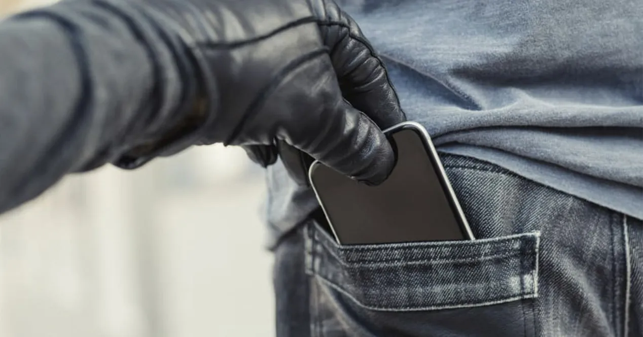 Main avec un gant en cuir noir sortant un téléphone portable de la poche arrière d'un jean.