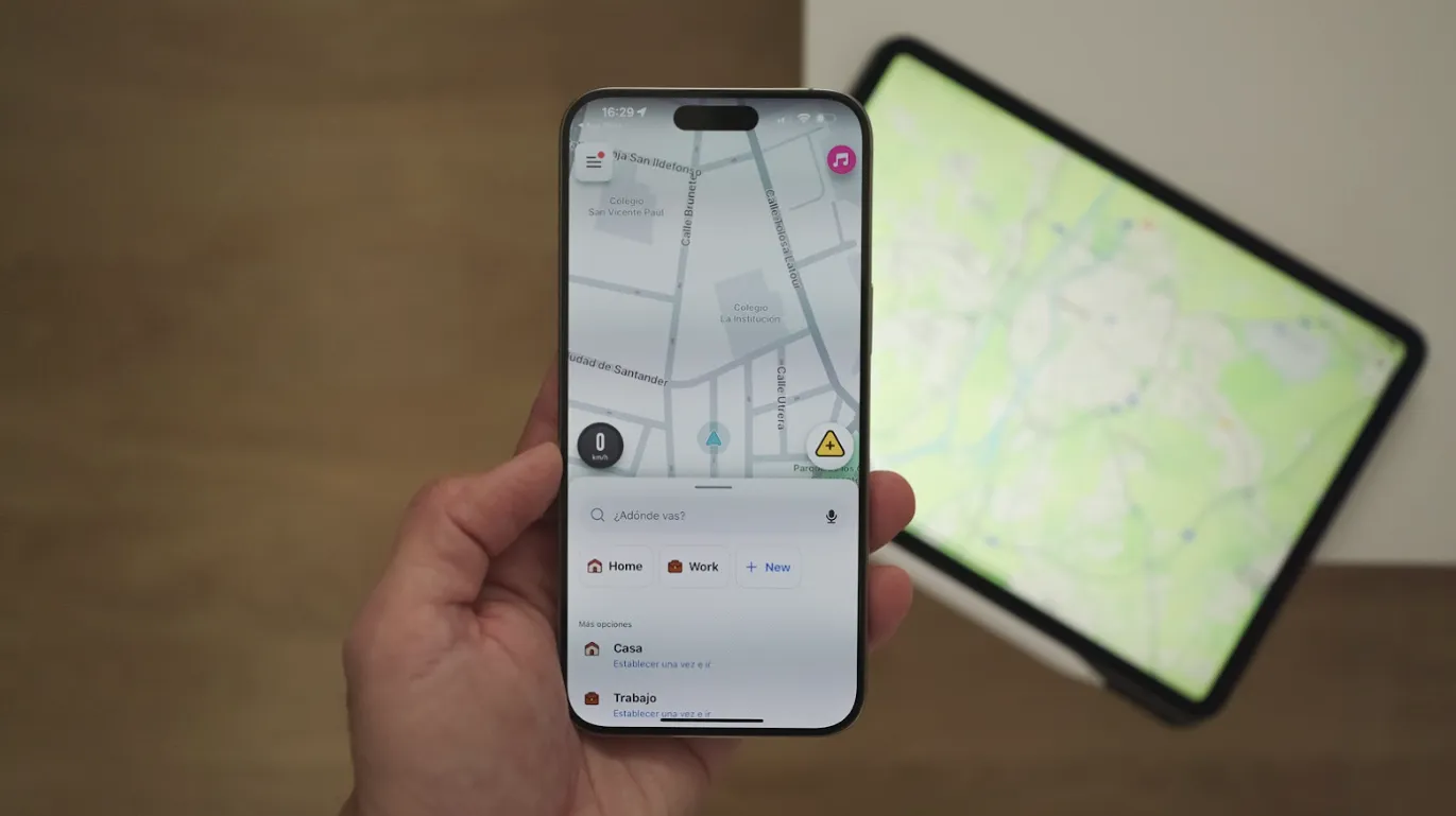 Interface de l'application Waze ouverte sur un iPhone tenu dans une main, avec une tablette affichant une carte en arrière-plan.