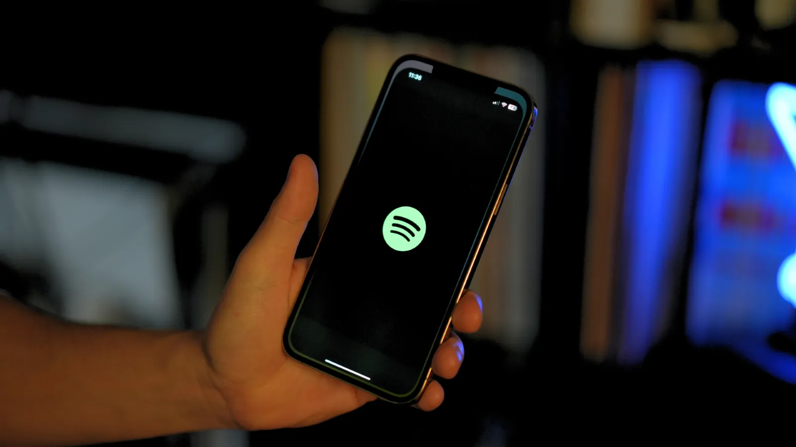 Mano sujetando un teléfono móvil con el logotipo verde de Spotify centrado en la pantalla negra.